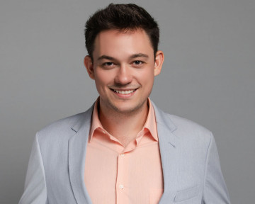 Confident young man in blazer smiles warmly, showcasing professionalism and approachability.